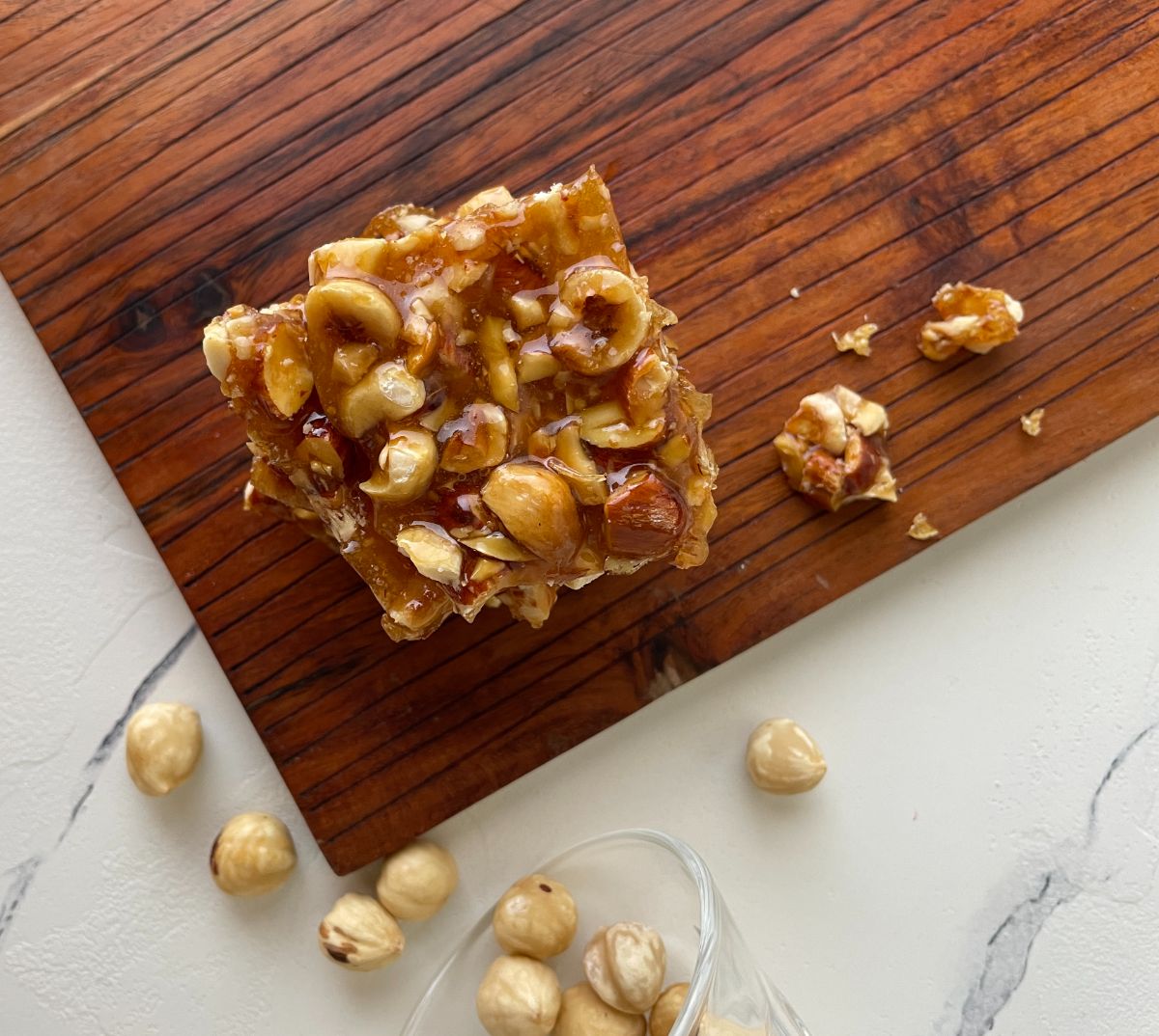 a piece of krokan on a wooden platter with nuts in the background