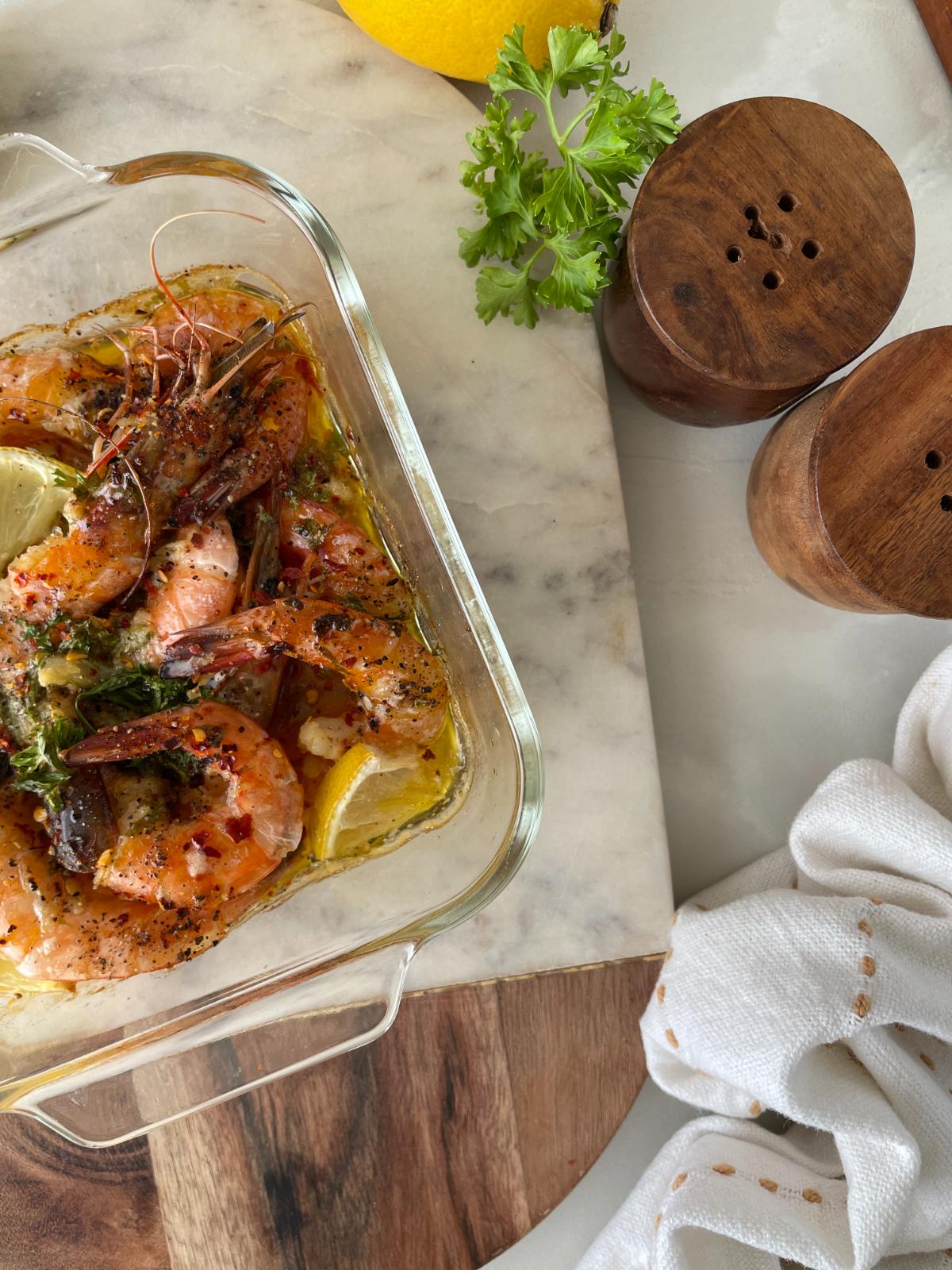 garlic lemon butter shrimp in a baking dish with seasonings and ingredients on the side