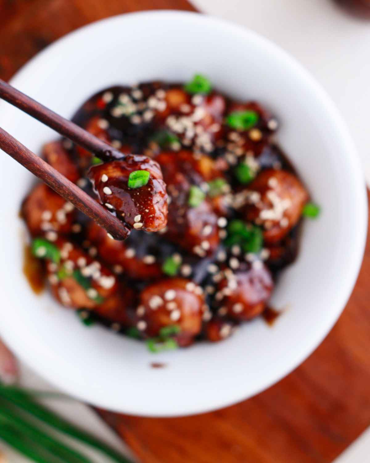 Chop sticks holding a piece of Teriyaki Chicken from the bowl