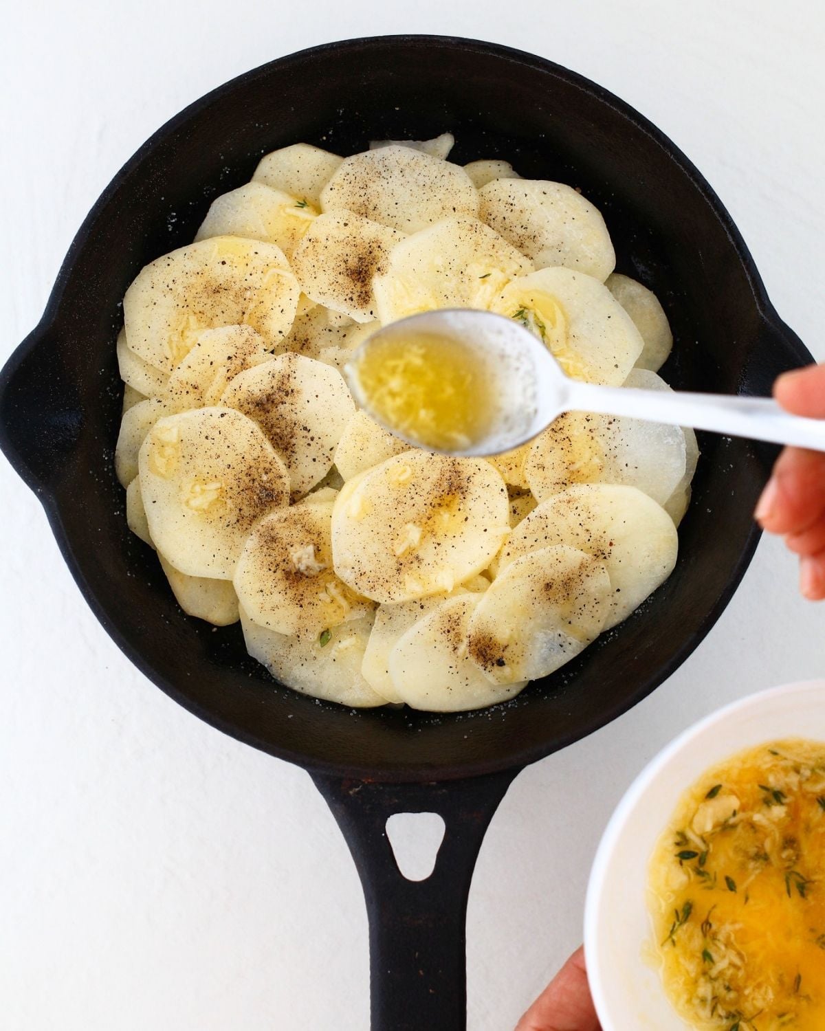 Garlic butter being spooned over seasoned potato slices